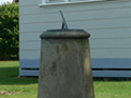 Sundial on concrete plinth in front of wooden church building